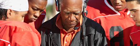 African American coach with headset in the middle of a huddle