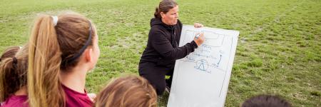 Girls looking at female coach writing on whiteboard during planning form soccer match on sports field