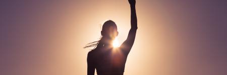 silhouette of a woman standing in the sunset with her right fist in the hair